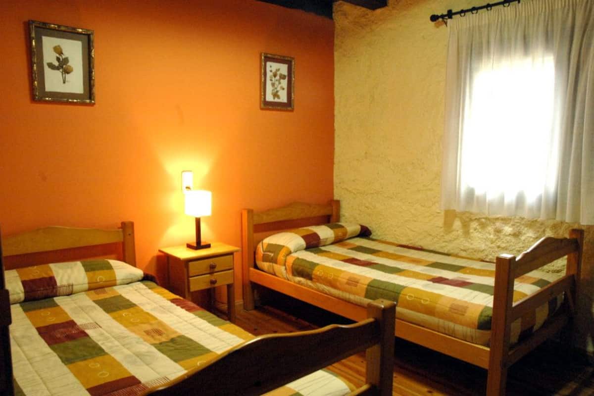 A room with two wooden beds, a nightstand, a lamp, and a window with curtains.