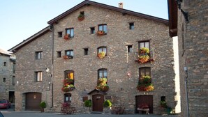 A stone building with multiple windows, some with flower boxes. There are outdoor seating areas in front. - Albergue Rural Ca L'anton (Sort)