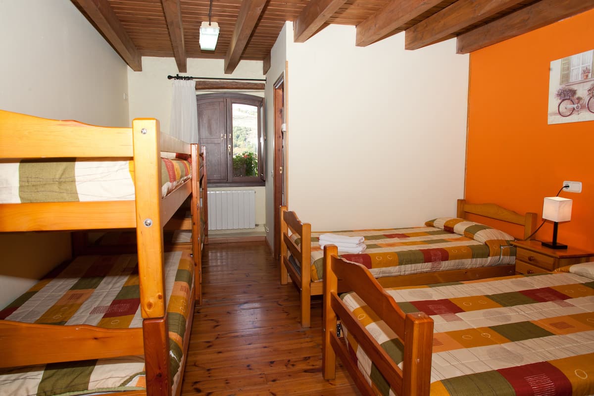A room with three wooden bunk beds, a wooden floor, a window with curtains, and an orange wall.