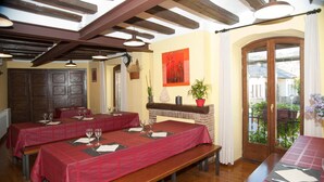 A dining area with wooden tables and benches, red tablecloths, and a view through a glass door to the outside. - Albergue Rural Ca L'anton (Sort)