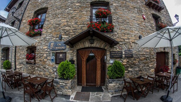 A stone building with a wooden door, outdoor seating, and flower boxes. - Albergue Rural Ca L'anton (Sort)