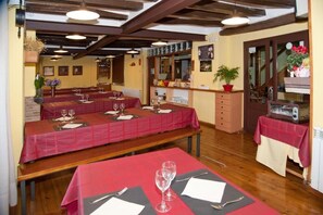 A restaurant with multiple tables set for dining, wooden beams on the ceiling, and a counter with various items.