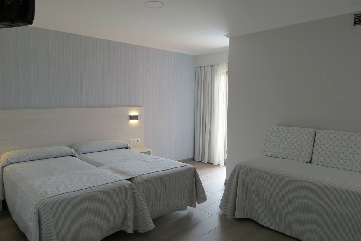 Una habitación de hotel con dos camas, una mesita de noche y una lámpara fijada a la pared.