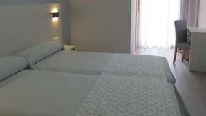 Habitación de hotel con dos camas, un escritorio, una silla y un ventanal con cortinas.