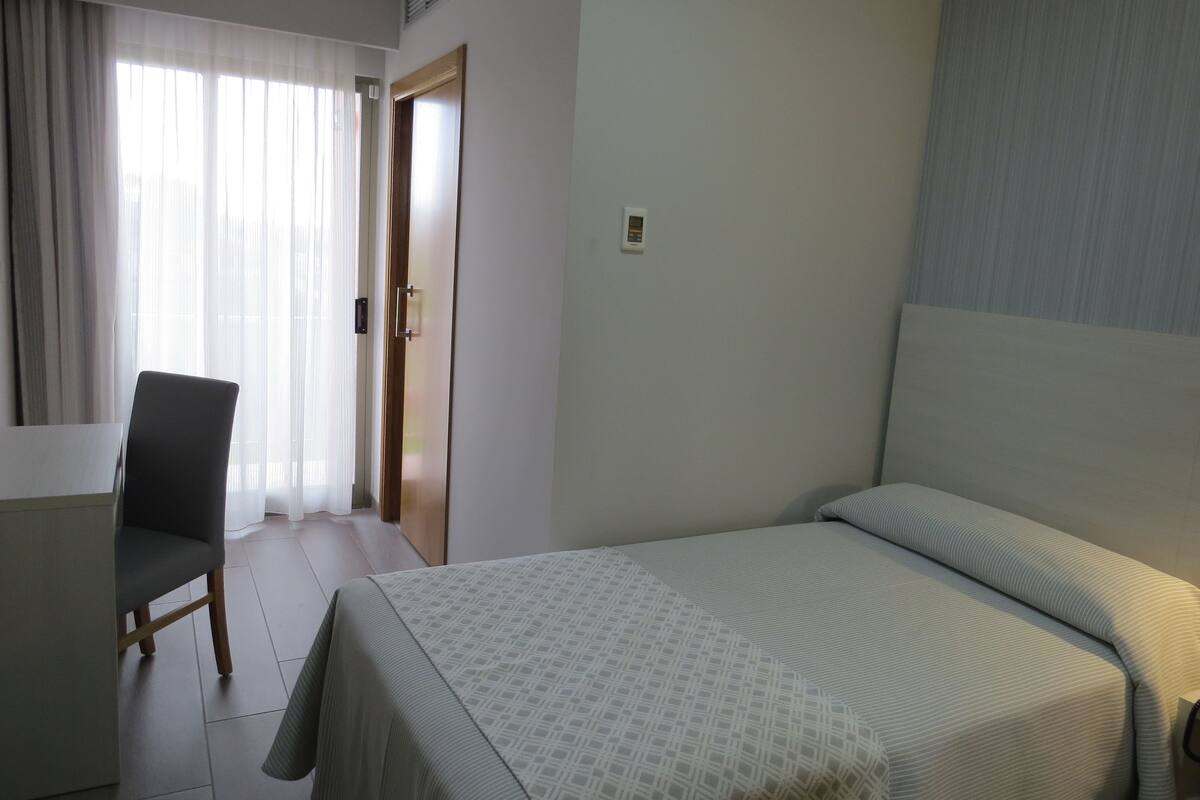 Una habitación de hotel con una cama, una silla, un escritorio y una puerta.