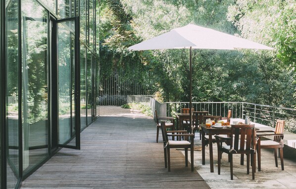 An outdoor deck with glass walls, wooden flooring, and a table with chairs and an umbrella. - Fuente Ace ña Hotel Boutique (Quintanilla de Onesimo)