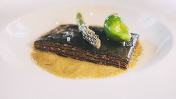 Un postre en un plato con una base de chocolate brillante, una fruta verde y un detalle decorativo.