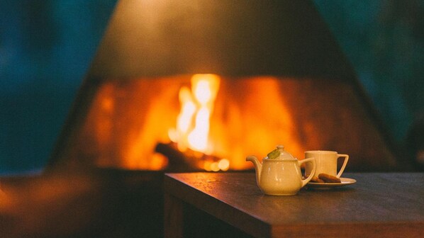 A table with a teapot and a cup in front of a fireplace with a visible fire. - Fuente Aceña Hotel Boutique (Quintanilla de Onesimo)