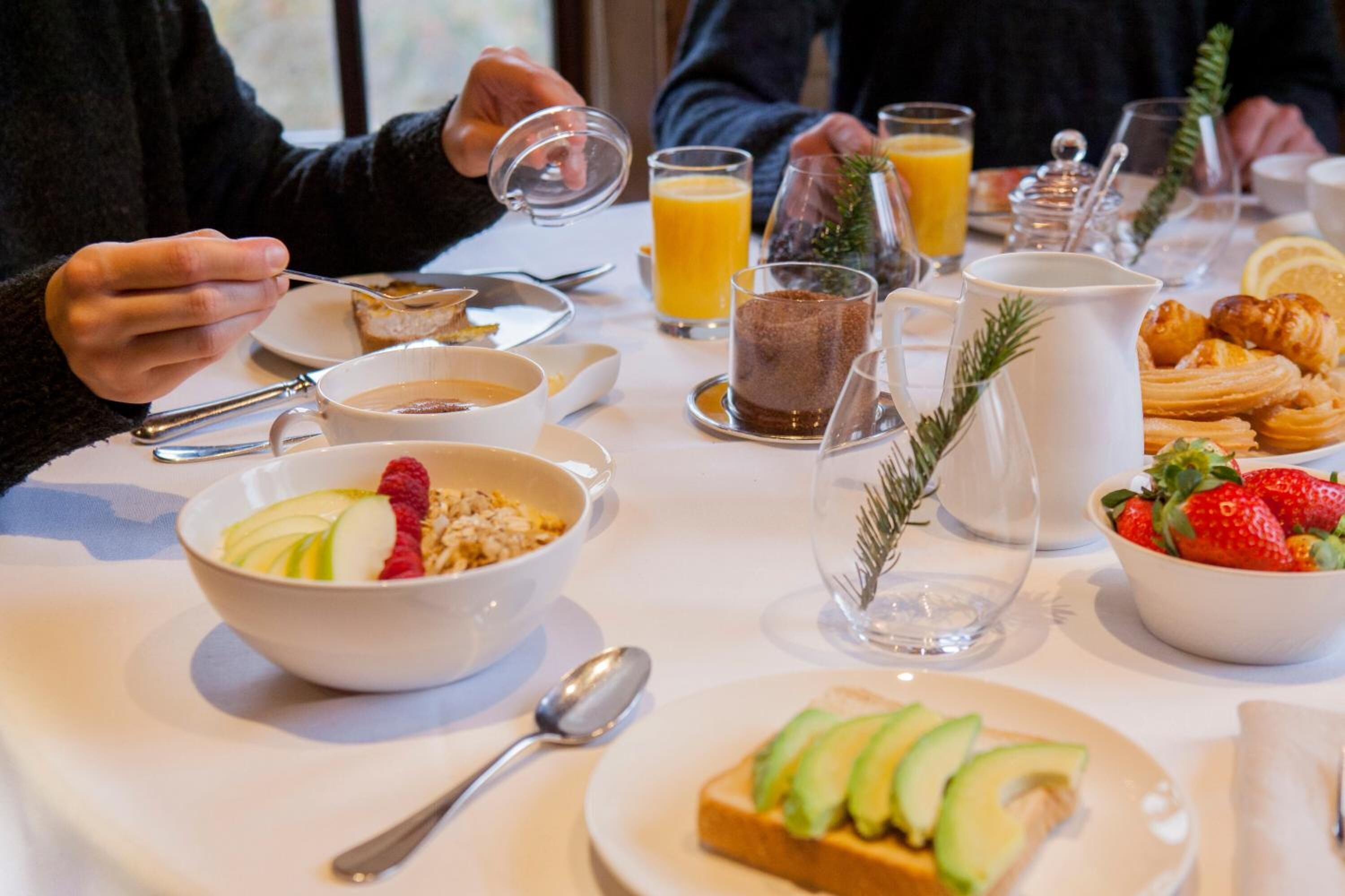 Een ontbijttafel met diverse gerechten, waaronder een kom cerealkorrels met aardbeien, een glas sinaasappelsap en croissants.