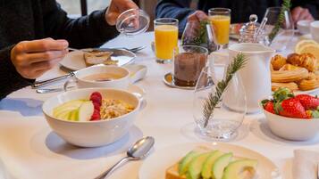 Un desayuno con diversos platos, incluyendo un tazón de cereal con fresas, un vaso de jugo de naranja y cruasanes.