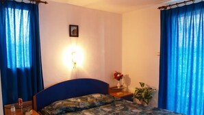 Quarto com cama, mesa de cabeceira, luminária e cortinas.