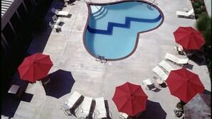 Una piscina en la azotea con forma de corazón, rodeada de sillones de descanso y sombrillas rojas.