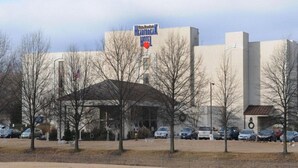 Un hotel con un letrero grande, un acceso cubierto y un estacionamiento con coches.