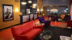 Un vestíbulo de hotel con un sofá rojo, sillas moradas, un mostrador de recepción y una pantalla de televisión.
