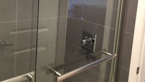 A modern shower with a glass door, a handheld showerhead, and a control panel.