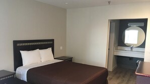 A hotel room with a large bed, a nightstand, a dresser, and a bathroom with a sink and mirror.