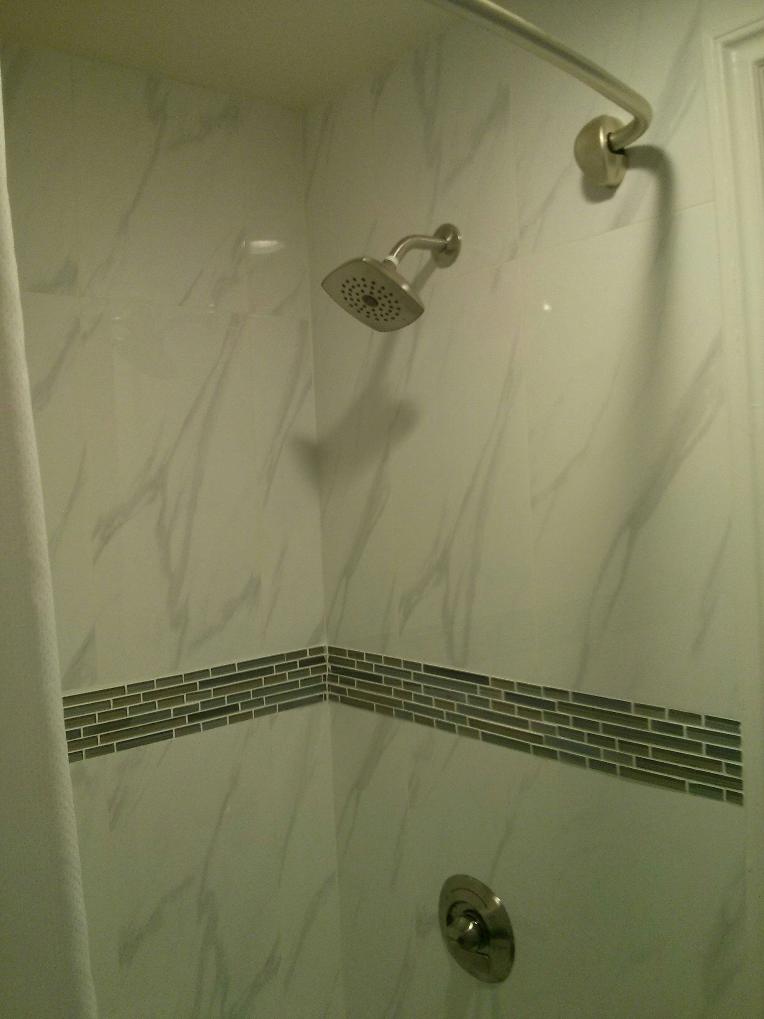 A shower with a handheld showerhead and a corner tile design.