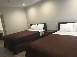 Una habitación de hotel con dos camas individuales, cada una con cubrecama marrón y almohadas blancas. La habitación tiene una distribución sencilla, con una mesita de noche entre las camas y una pequeña mesa.
