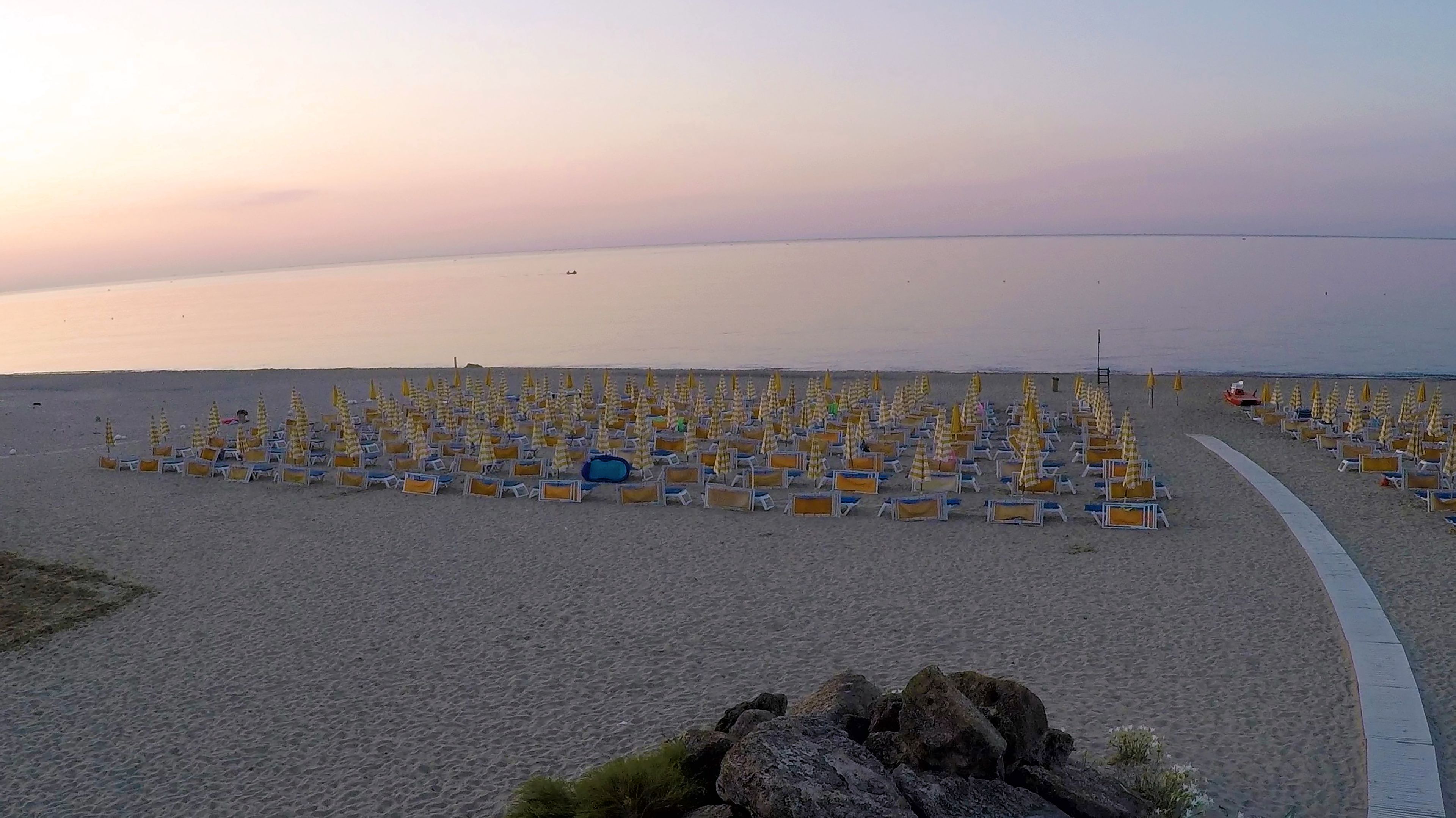 A beach with rows of sun loungers and umbrellas, a clear sky, and a calm sea.