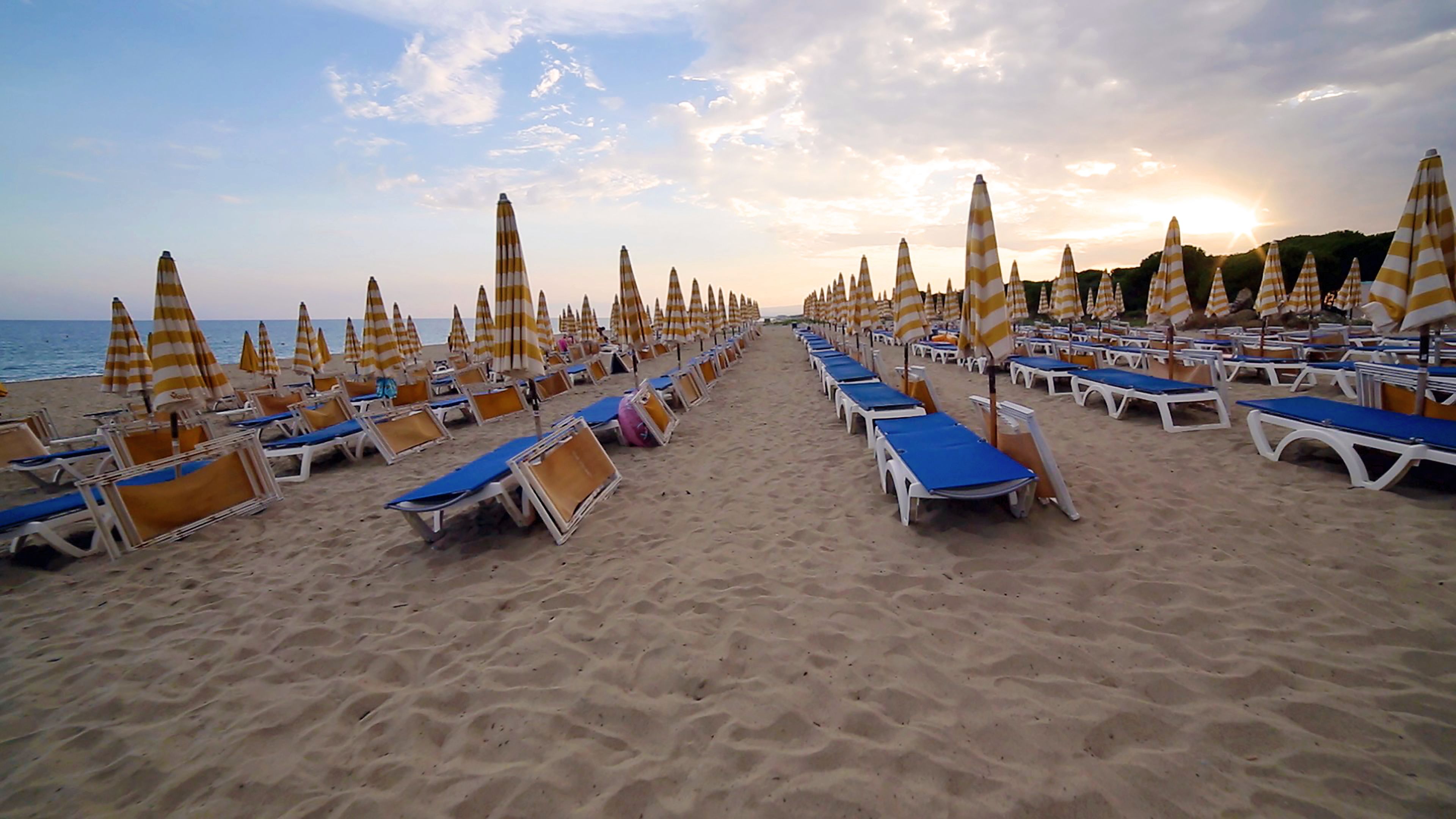 Une plage bordée de rangées de chaises longues et de parasols à rayures, donnant sur la mer.