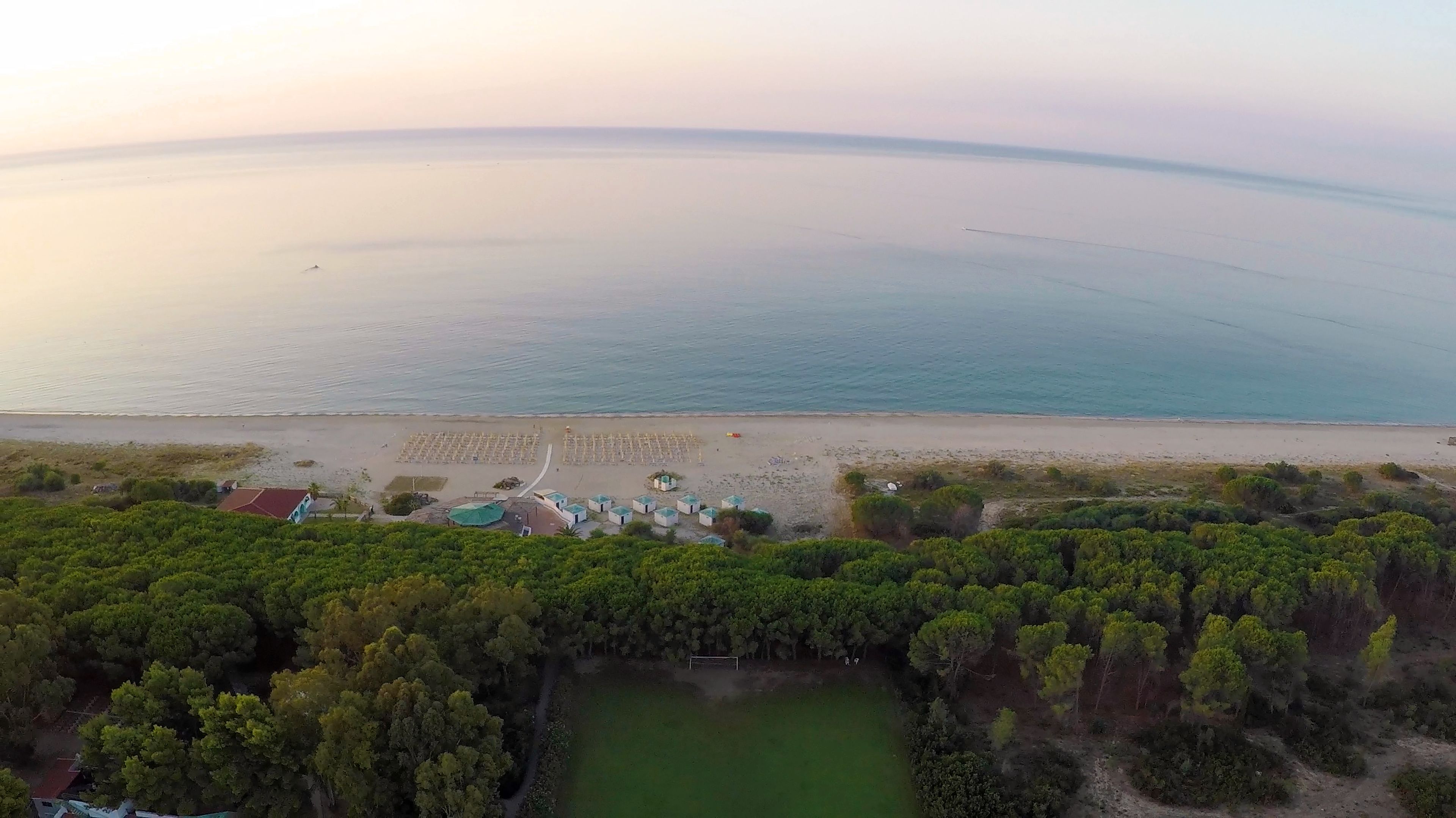 Eine Vogelperspektive auf eine Küstenlandschaft mit Strand, einer Reihe Strandkörbe und dicht bewaldetem Land.