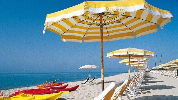 A beach with rows of yellow and white striped umbrellas, beach chairs, and canoes lined up on the sand. - Villaggio Triton - Aurum Hotels (Sellia Marina)