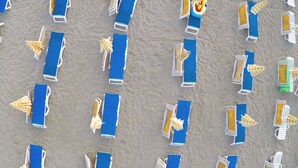An aerial view of a beach with rows of blue lounge chairs and yellow-striped umbrellas. - Villaggio Triton - Aurum Hotels (Sellia Marina)