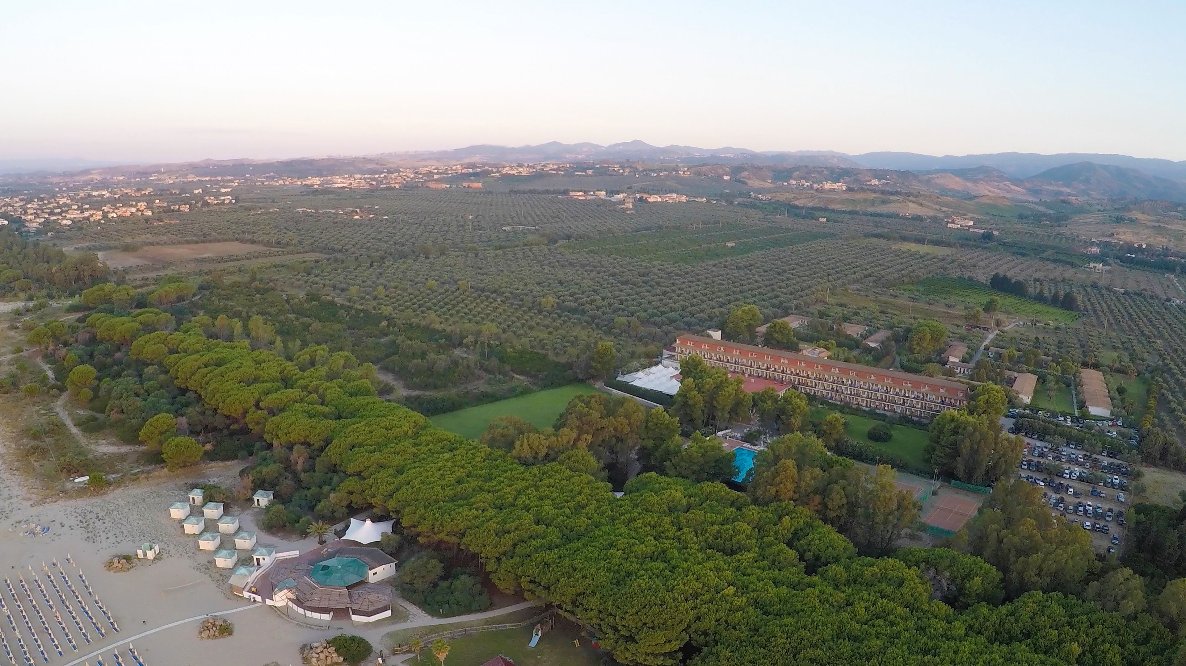 Vue aérienne d’un complexe hôtelier comprenant une piscine, des villas pour les clients et un grand bâtiment doté d’un toit rouge.
