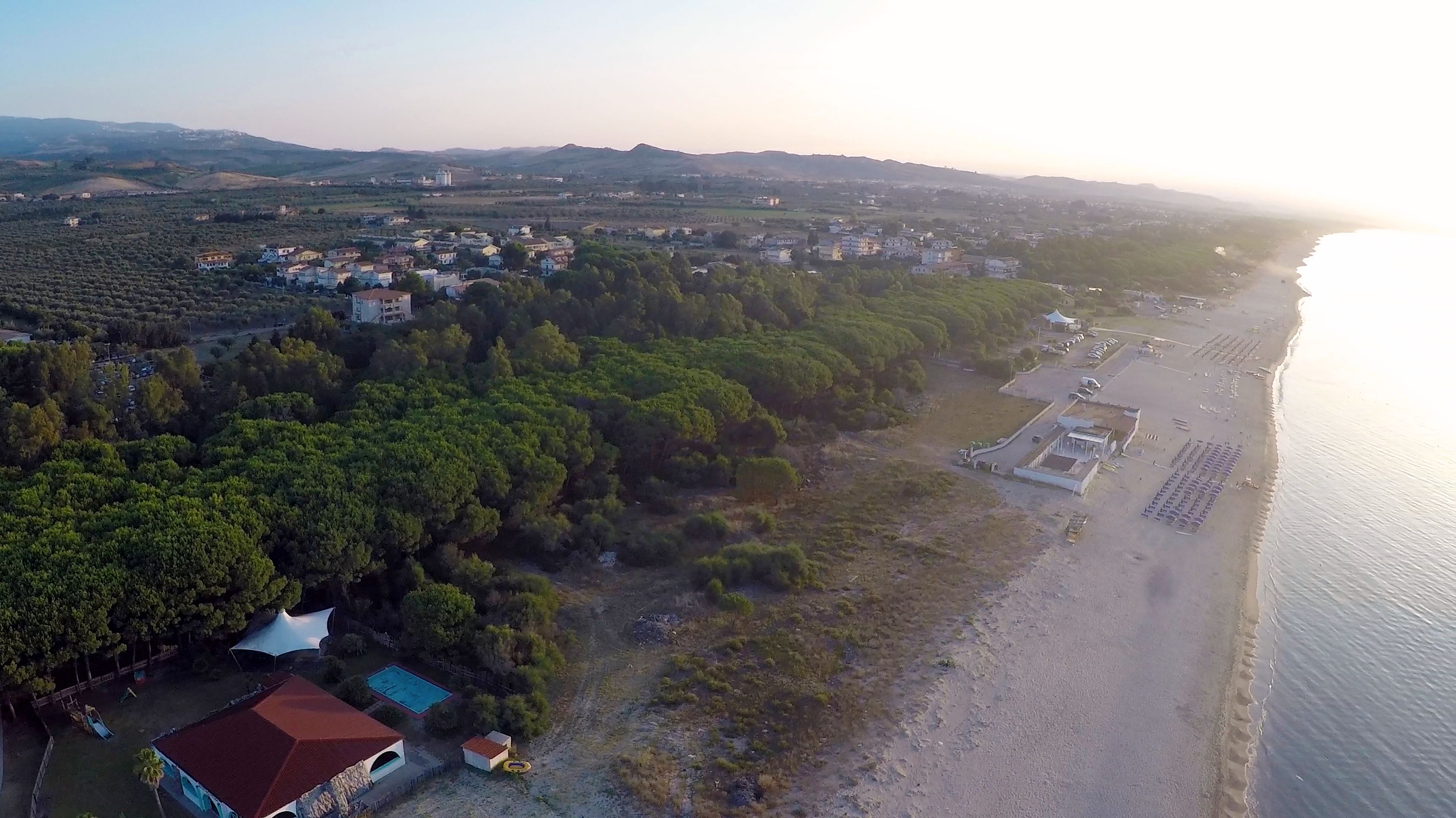 An aerial view of a coastal area with residential buildings, a beach, and a swimming pool.
