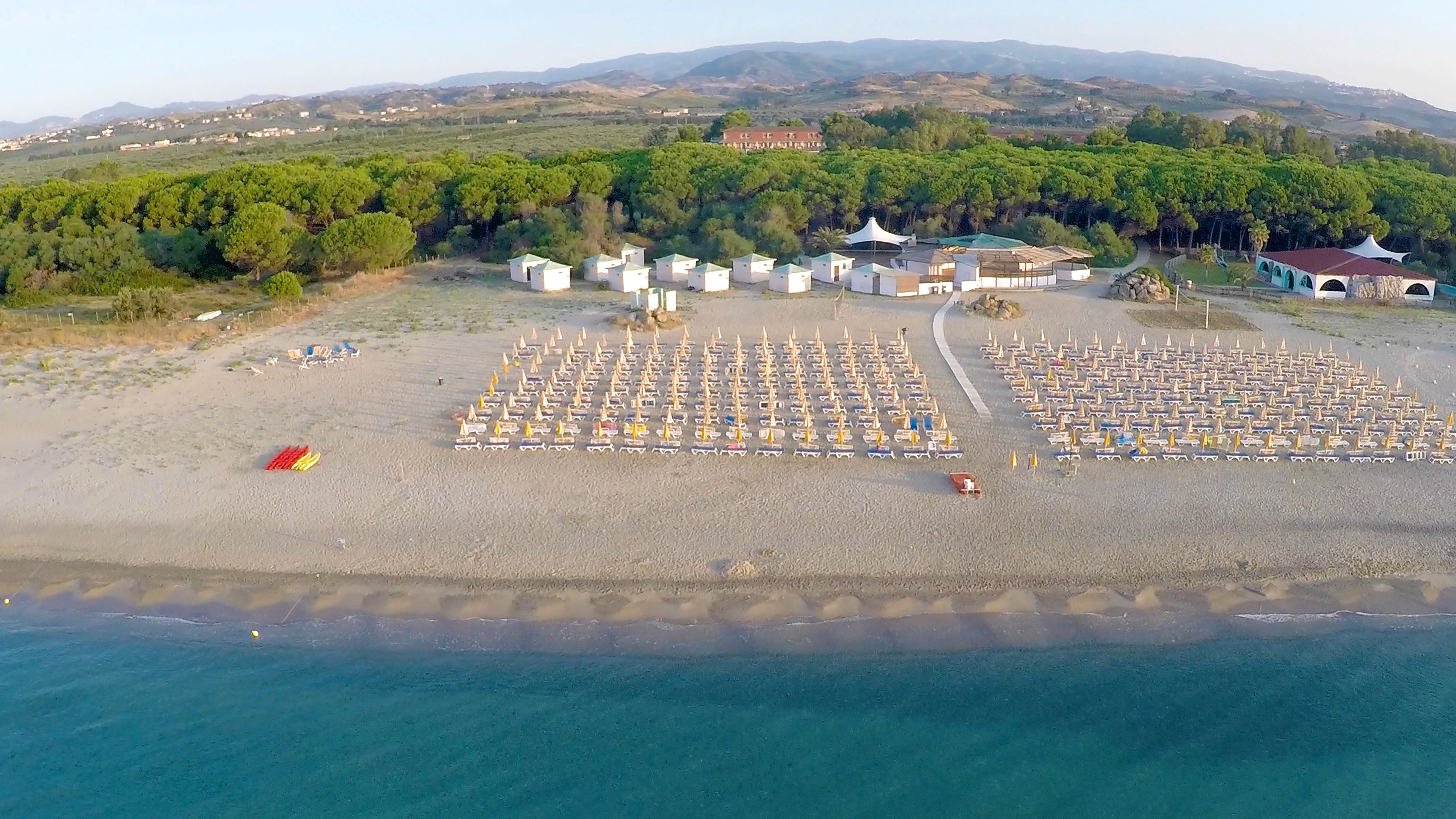 An aerial view of a beach with rows of beach umbrellas and small beach huts.