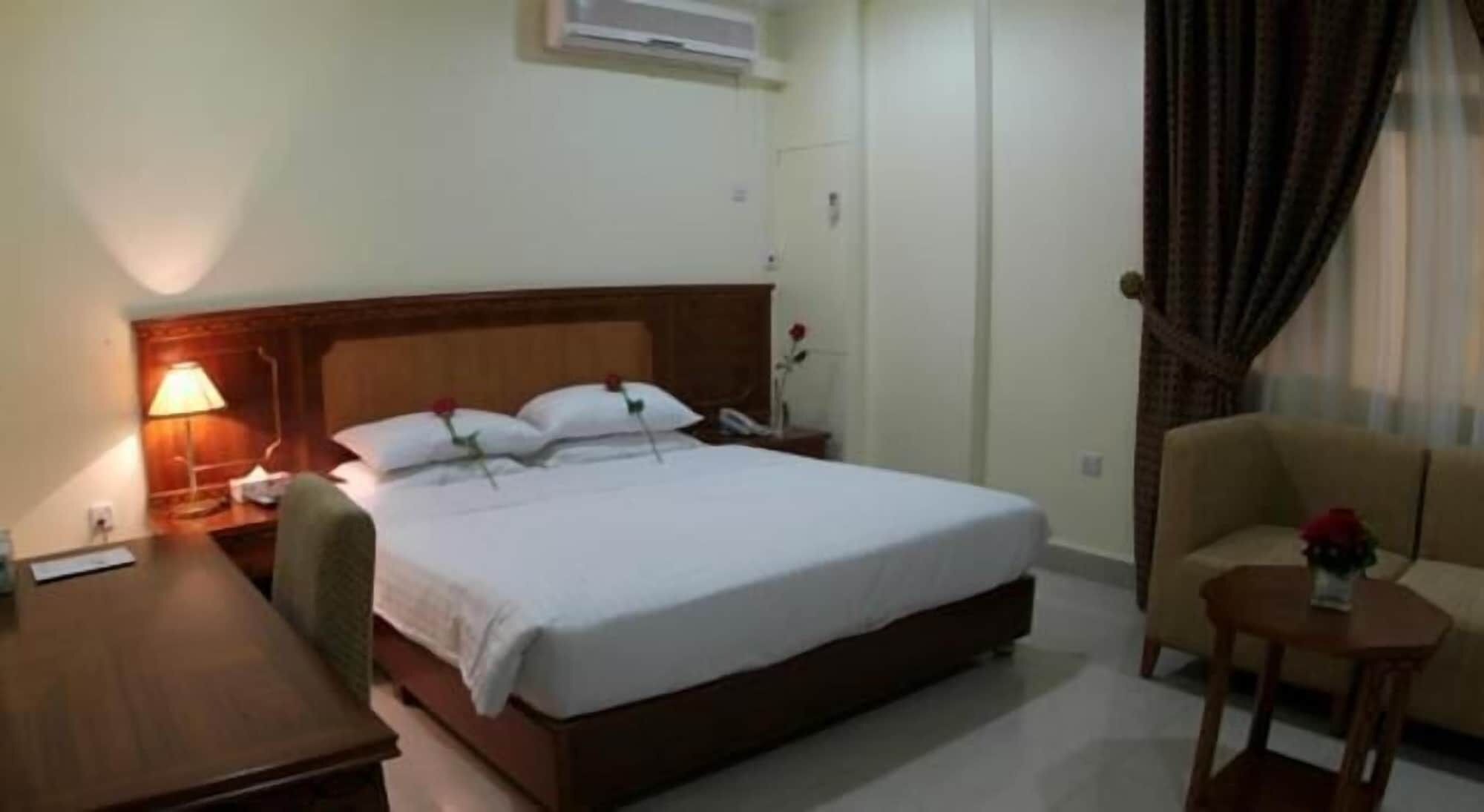 A hotel room with a large bed, a desk, a chair, a small table with a vase of flowers, and a sofa.