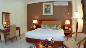 Ein Hotelzimmer mit einem großen Bett, zwei Nachttischlampen, einem Schreibtisch mit Stuhl, einem Spiegel und einer Obstschale auf dem Nachttisch.