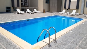 Ein rechteckiger Swimmingpool mit klarem, blauem Wasser, umgeben von einer gefliesten Terrasse.