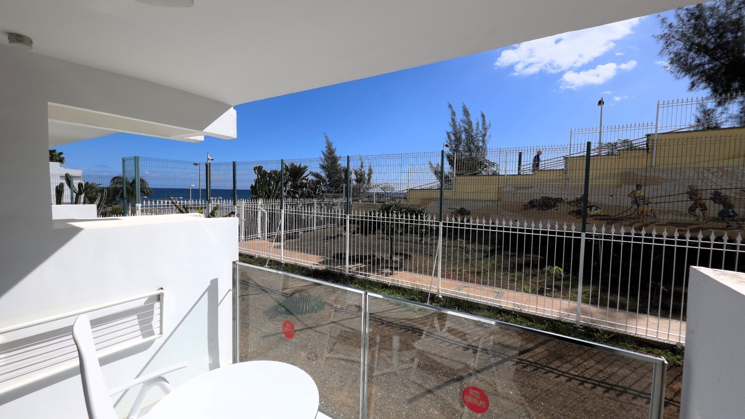 Uma varanda com vista para uma área externa cercada, incluindo uma piscina e um edifício ao fundo.