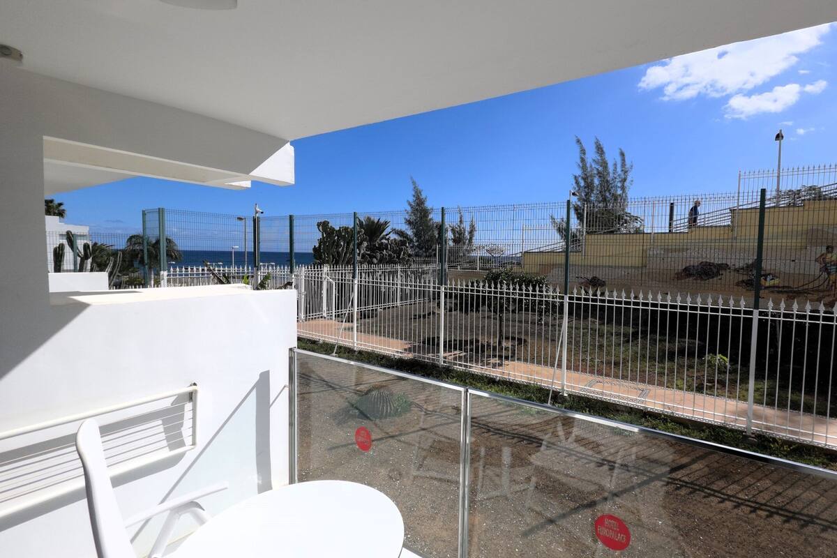 Ein Balkon mit Blick auf einen eingezäunten Außenbereich, einschließlich eines Pools und einem Gebäude im Hintergrund.