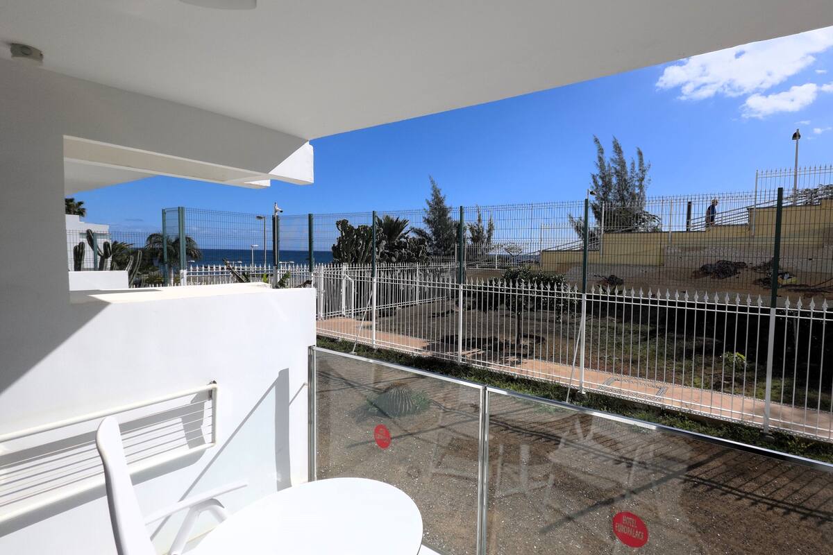 Ein Balkon mit Blick auf einen umzäunten Außenbereich, der einen Pool und ein Gebäude mit gelber Fassade zeigt.