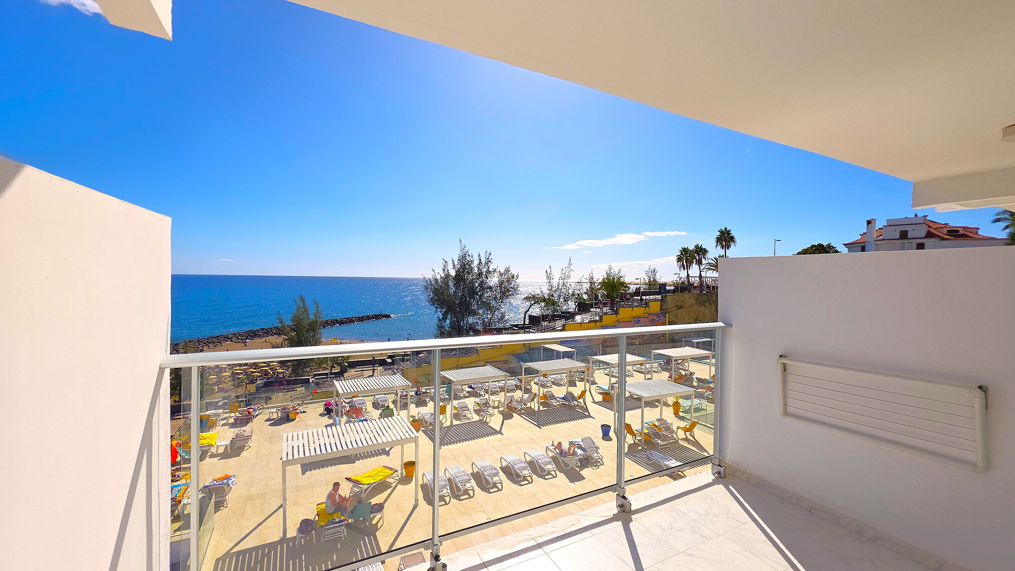 A balcony with a view of a beach, sun loungers, and a clear blue sky.