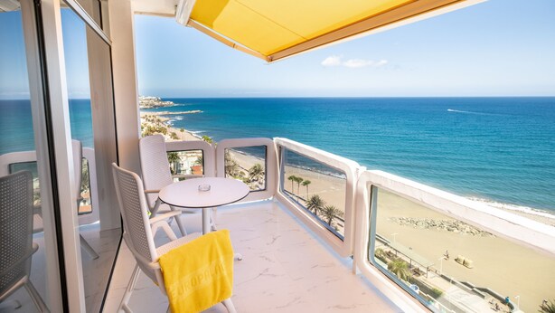 A balcony with a view of the sea and beach, featuring a table and chairs, and a yellow umbrella. - Europalace (San Bartolomé de Tirajana)