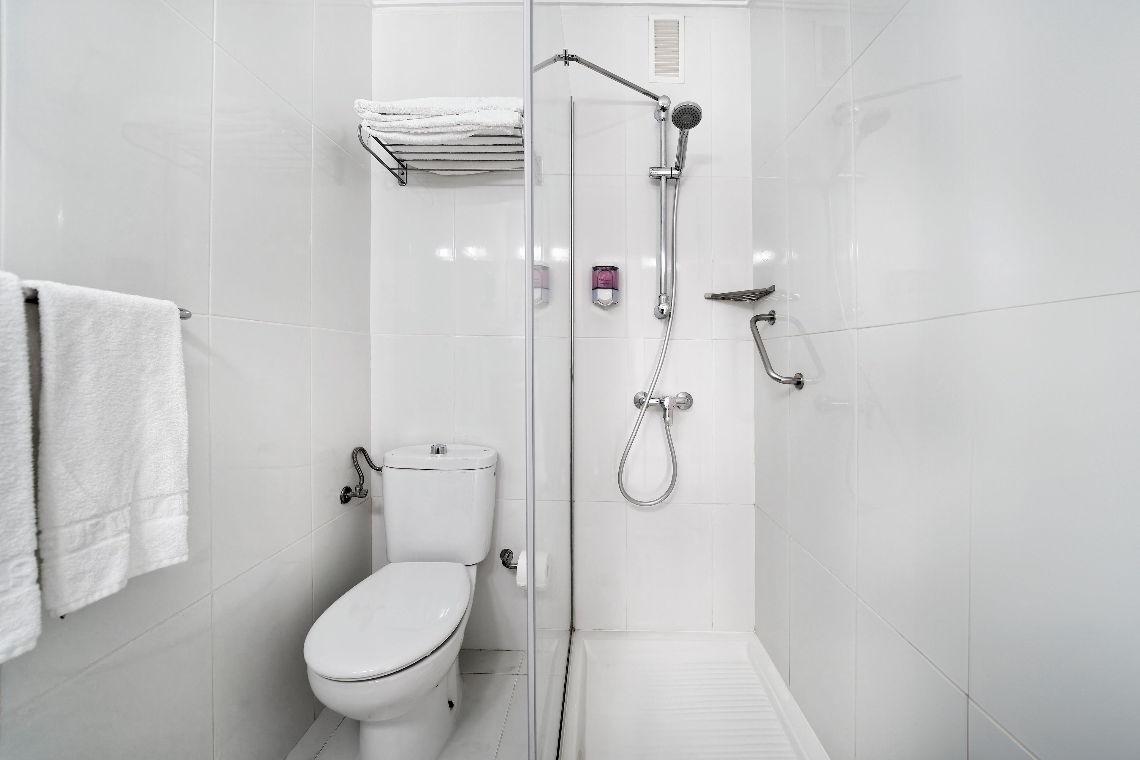 Een moderne badkamer met toilet, douche met glazen wand en een handdoekhouder.