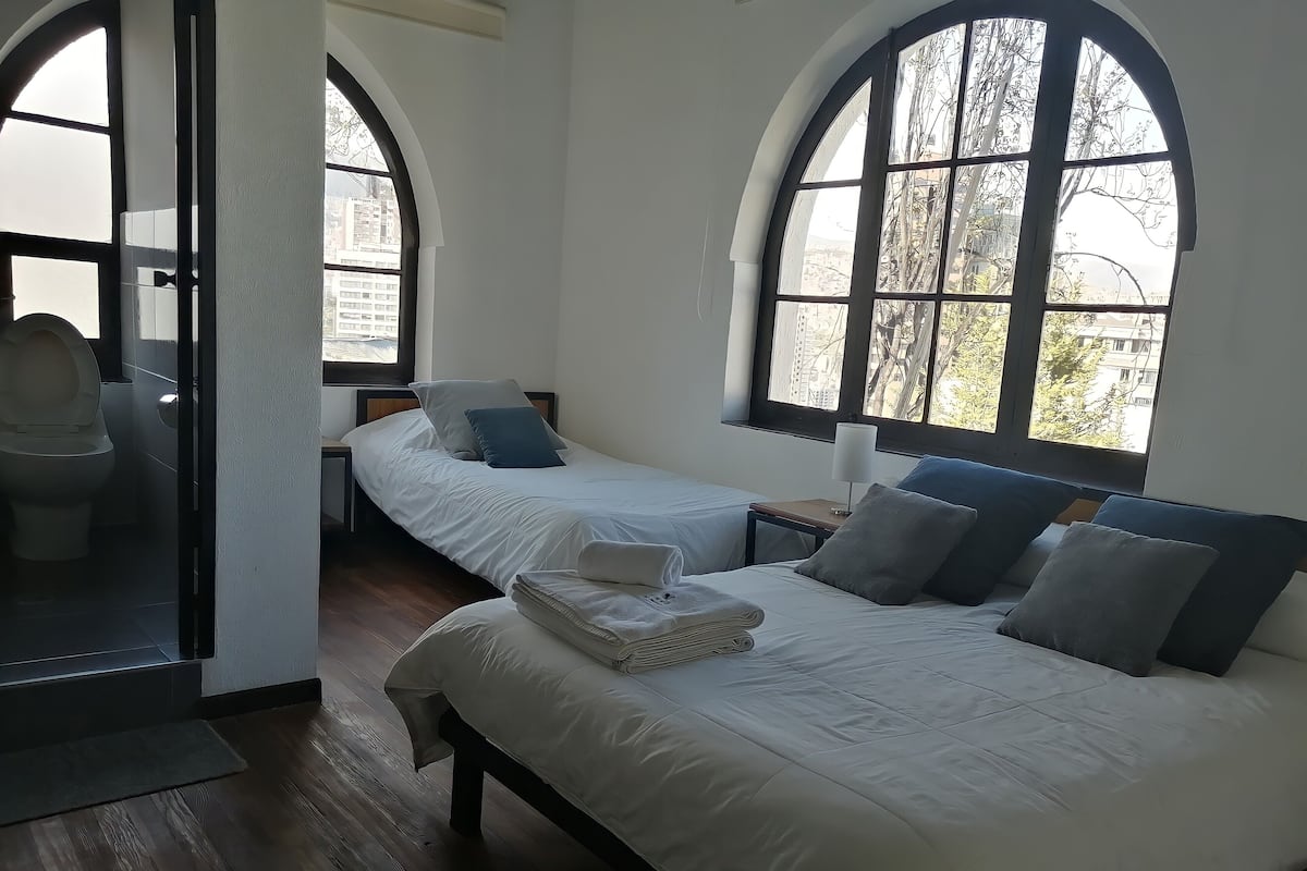 A hotel room with two beds, a bathroom, and large arched windows.