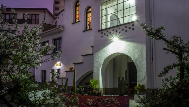 A building with arched windows and a central archway, surrounded by flowering plants and cacti. - El Museo Hotel Boutique (La Paz)