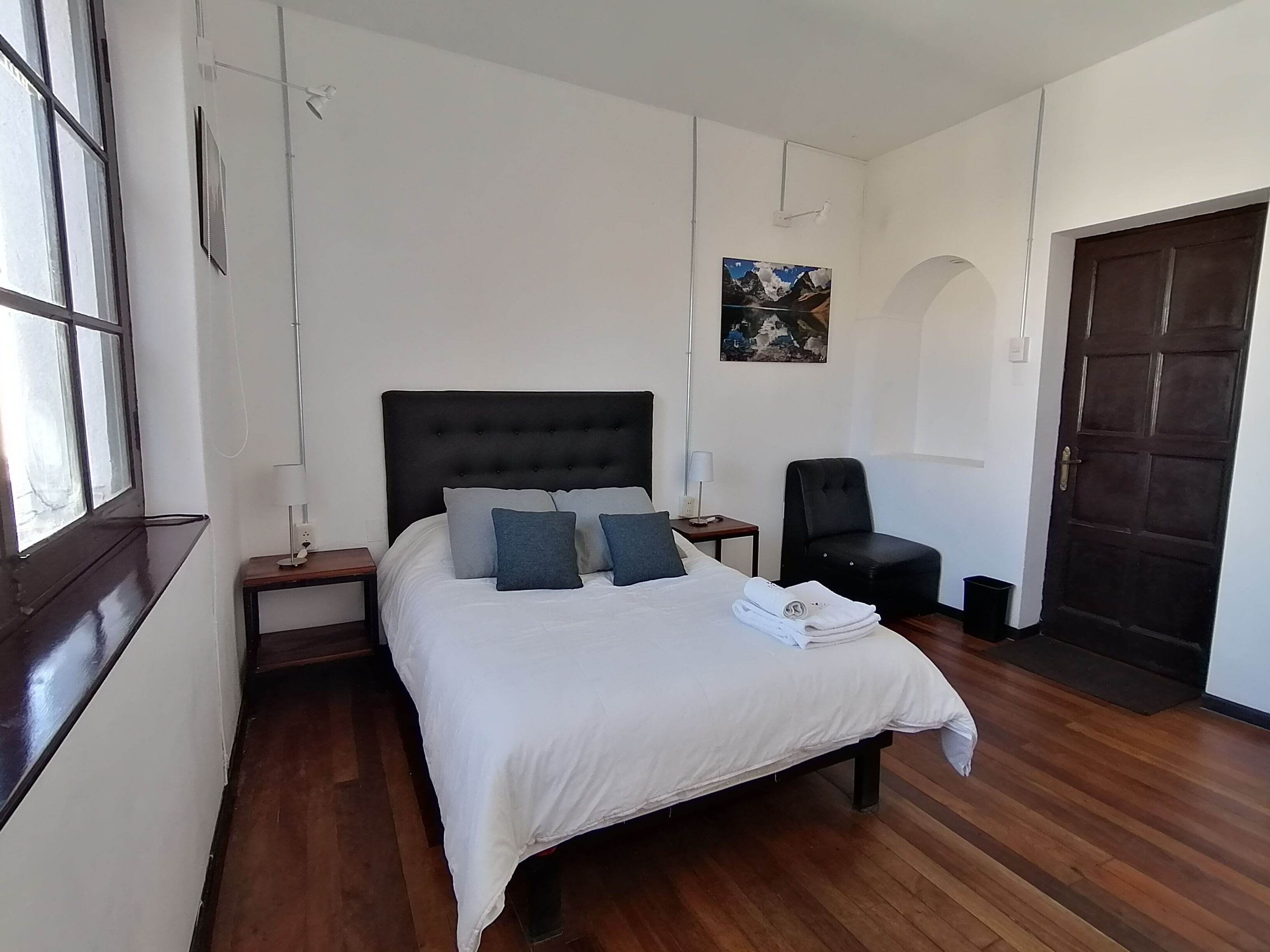 A neatly arranged bedroom with a large bed, a chair, a nightstand, and a door.