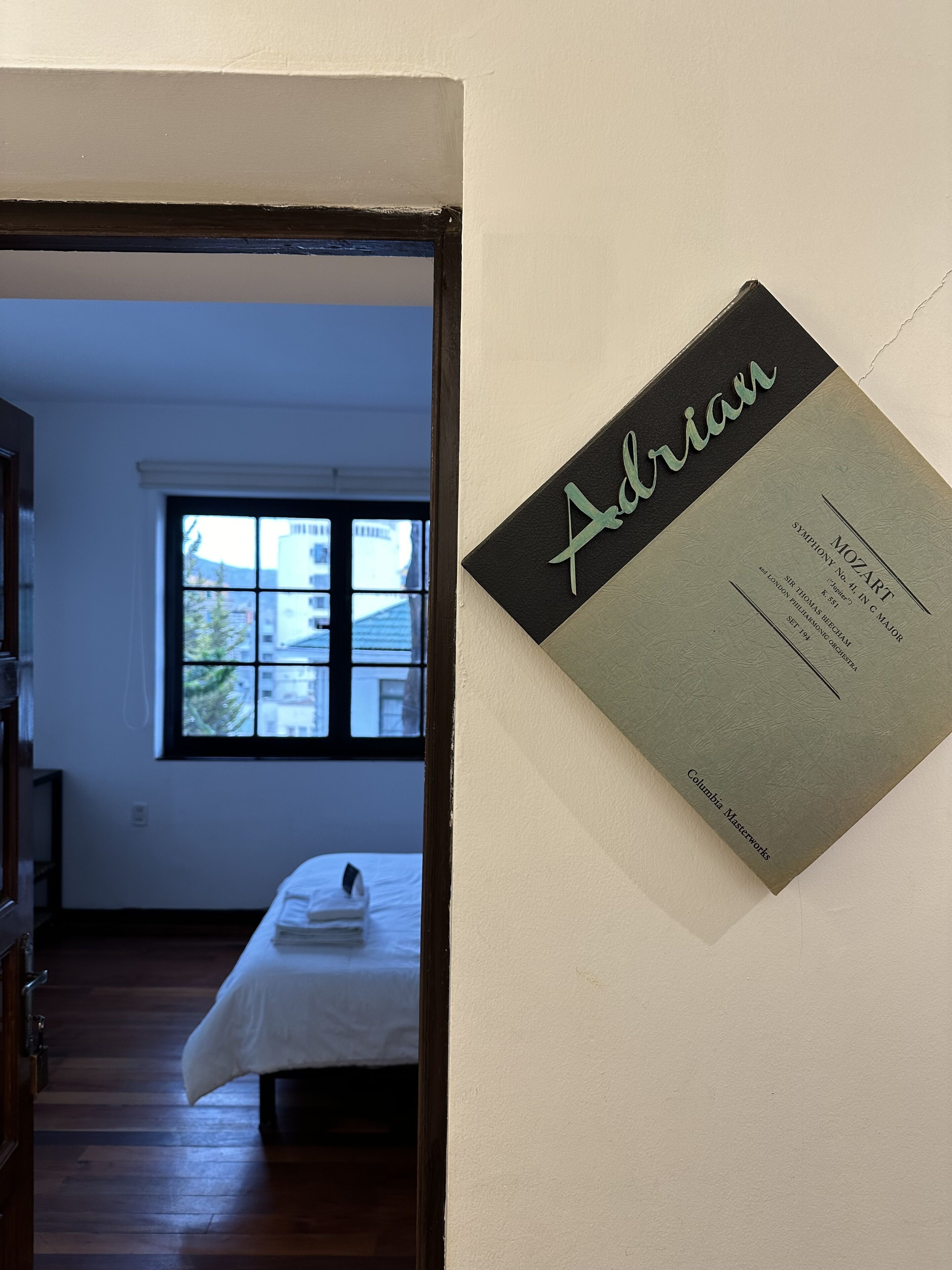Una habitación de hotel con una cama, un ventanal y un letrero en la pared que dice "Adrian".