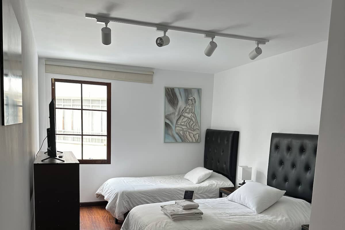 A bedroom with two beds, a desk, and a window.