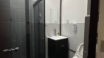 Un baño moderno con cabina de ducha de vidrio, un mueble de tocador oscuro y un inodoro.