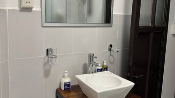 A bathroom with a white sink, a mirror, and a shower visible in the reflection.