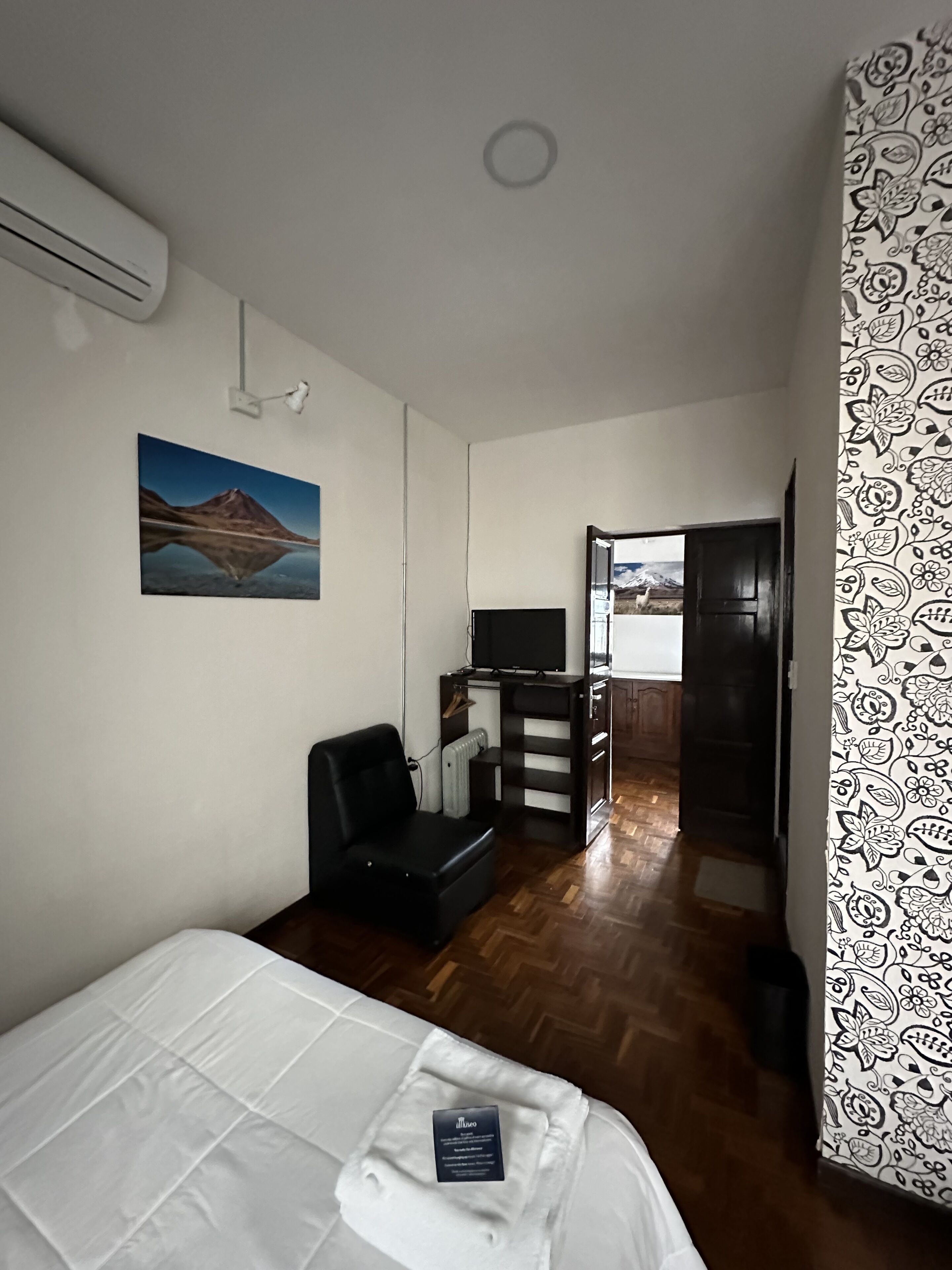 Una habitación de hotel con una cama, un escritorio con una computadora, una silla y un cuadro en la pared.
