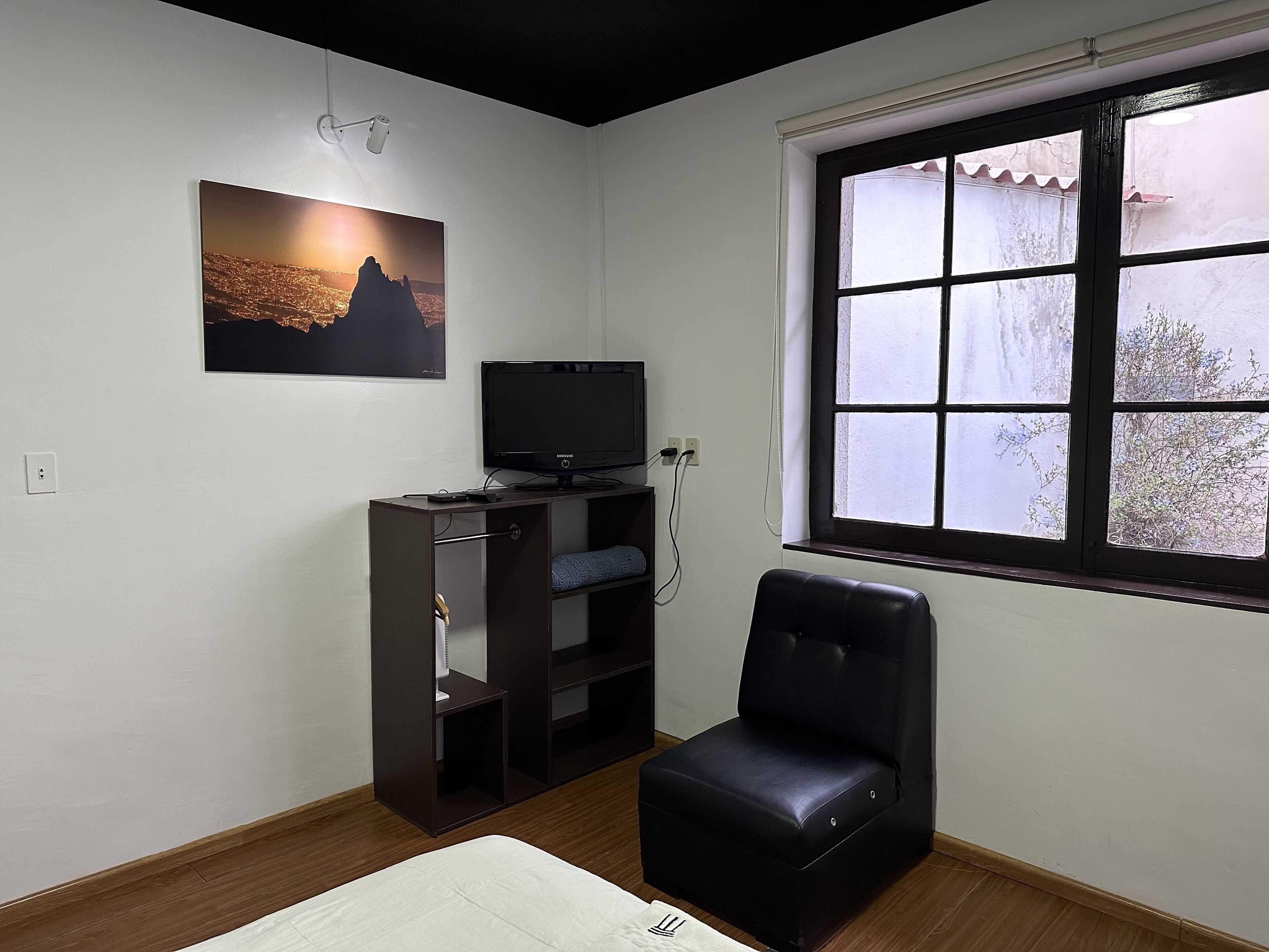 A room with a large window, a black leather chair, a TV on a wooden stand, and a framed picture on the wall.