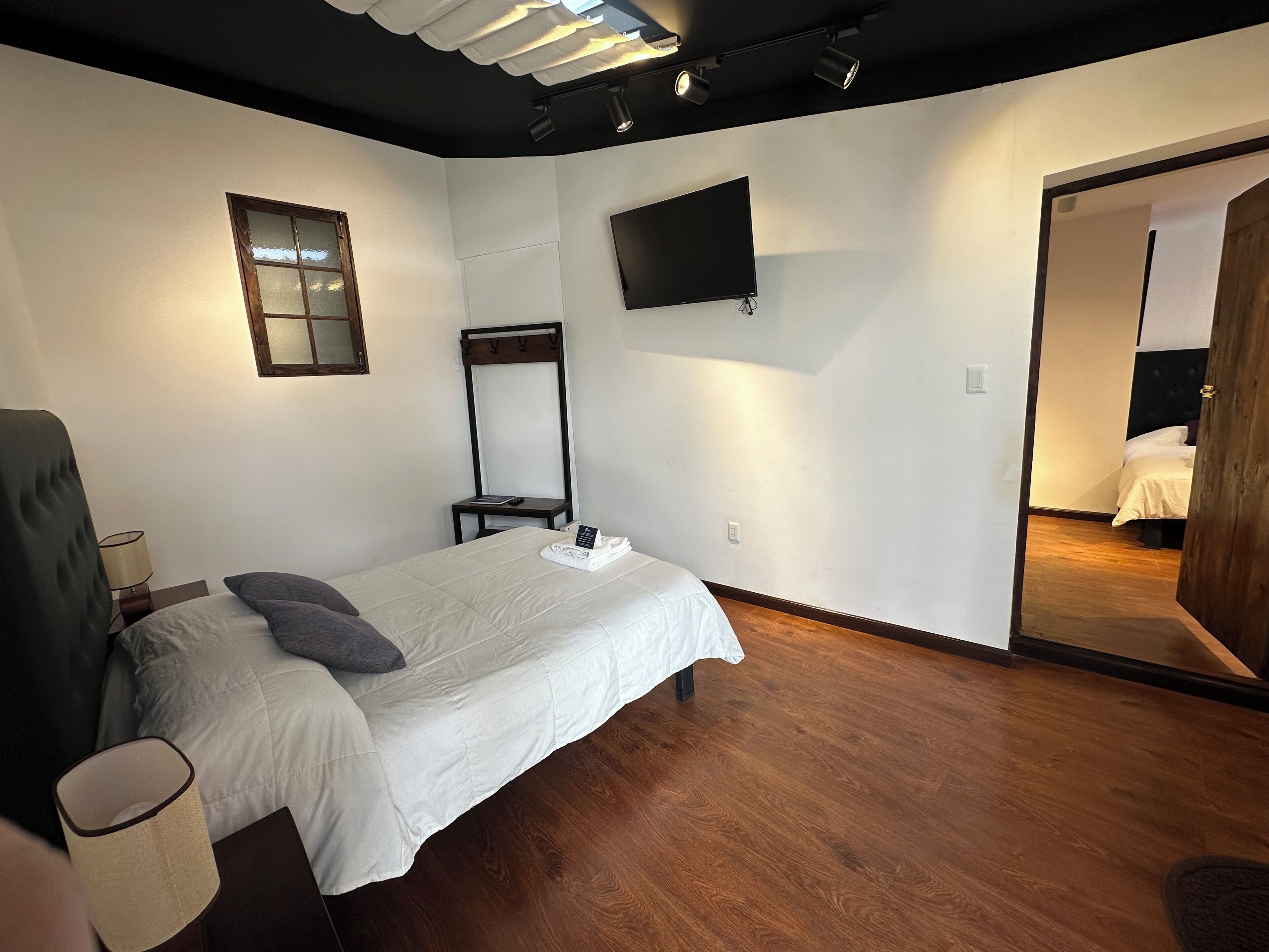 A bedroom with a bed, a bedside table, a lamp, a mirror, and a TV on the wall.
