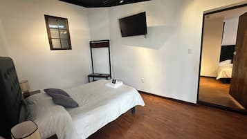 A bedroom with a bed, a bedside table, a lamp, a mirror, and a TV on the wall.